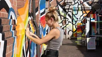 Person, die ein buntes Wandgemälde auf einer Backsteinmauer malt.