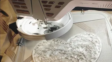 Nähmaschine stickt weißes Herzmuster.