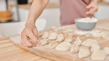 Person, die Knödel auf einem Holzbrett zubereitet.