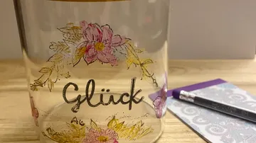 Glas mit „Glück“ und Blumenmuster auf dem Tisch.
