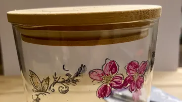 Glass jar with floral designs and wooden lid.