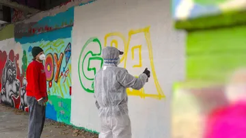 Person in suit spray painting graffiti wall.