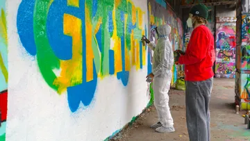 Two people spray painting colorful graffiti on wall.