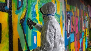 Person im Schutzanzug, die eine Graffiti-Wand besprüht.