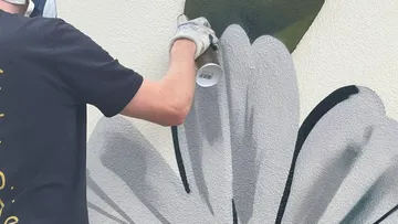 Person spray-painting gray flower mural.