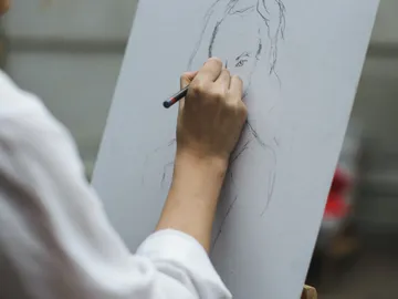 A hand draws a portrait on a canvas.