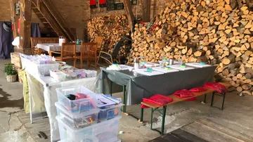 Tische mit Kunsthandwerk, Stapel Brennholz in der Scheune.