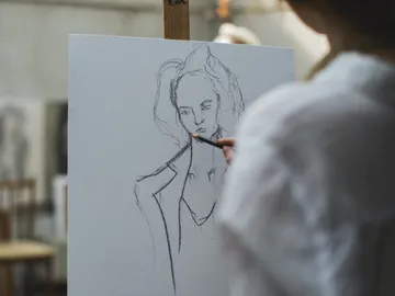A person draws a sketch of a woman on canvas.