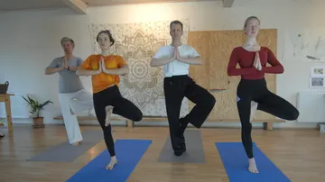 Vier Personen üben drinnen Yoga-Baum-Pose.