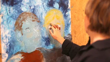 Artist painting two abstract faces on canvas.