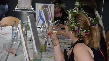 Frauen tragen Blumenkronen, malen und trinken Wein.