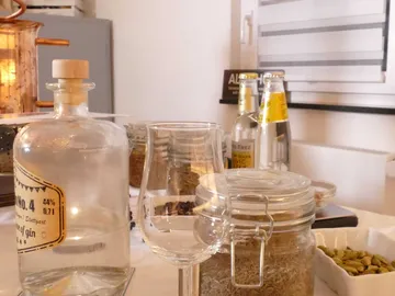 Glas steht neben Gin und Gewürzen auf einem Tisch.