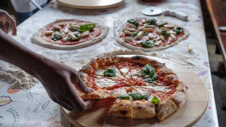 Hand holding pizza slice on preparation table.