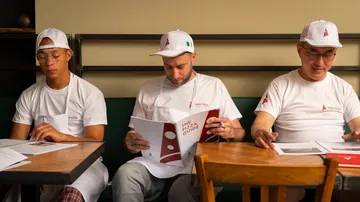 Drei Männer in weißen Uniformen lesen Pizzaführer