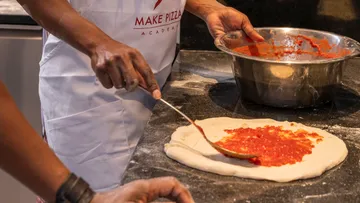 Person, die Tomatensauce auf Pizzateig verteilt.