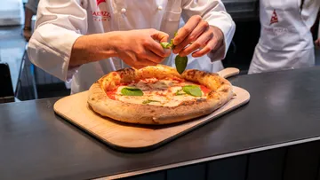 Der Koch fügt frisch gebackener Pizza Basilikum hinzu.