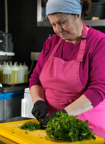 Woman chopping herbs on yellow board in kitchen.