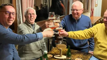 Four men toasting with beer glasses indoors.