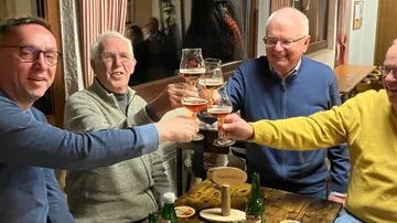 Four men toasting with beer glasses indoors.