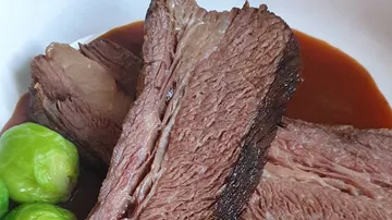 Sliced roast beef with gravy and Brussels sprouts.