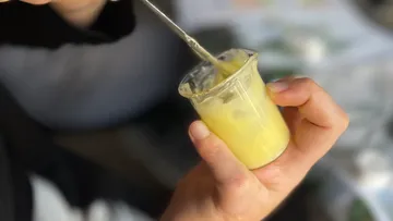 Hand holding yellow cream in small jar.