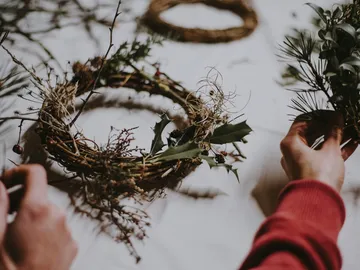 Hands make wreaths from plants on a table.