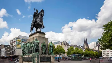 Equestrian statue in a city square, cloudy sky.