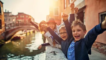 Joyful children raising arms near canal bridge.