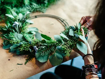 A person creates a wreath of green leaves.