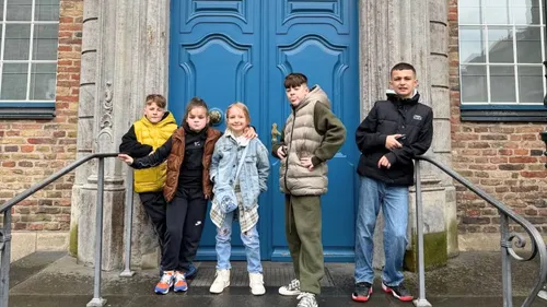 Fünf Kinder posieren vor einer blauen Tür.