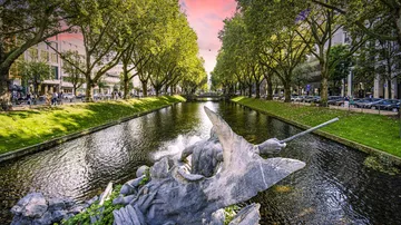 Skulptur in einem Kanal, umgeben von Bäumen und Gebäuden.