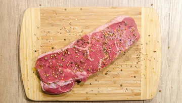 Gewürztes rohes Steak auf einem Holzschneidebrett.