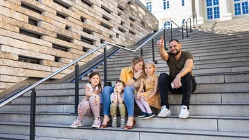 Family sitting on outdoor staircase, building facade.