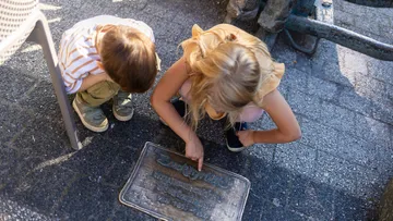 Two children examining engraved plaque on ground.