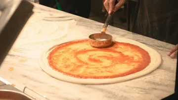 Person, die Tomatensauce auf Pizzateig verteilt.