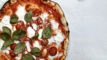 Pizza with basil, tomatoes, and cheese on table.