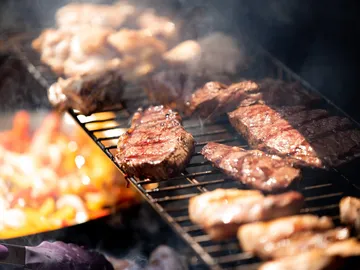 Fleisch grillt über einem Rost in rauchiger Umgebung.