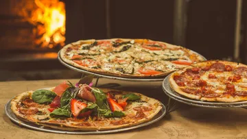 Three pizzas with various toppings near a fire.