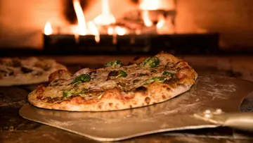 Pizza, die auf der Schale im Holzofen ruht.
