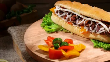 Grilled chicken sandwich with veggies on a board.