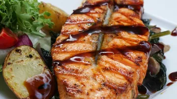Gegrillter Lachs mit Sauce und Gemüse auf einem Teller.