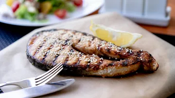 Grilled fish steak with lemon wedge, table setting.