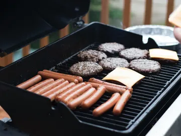 Grill mit Hamburgern und Würstchen in einer Außensituation.