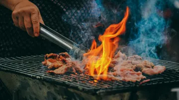 Person grilling meat over open flames.