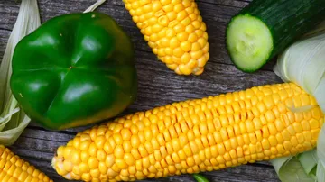 Corn, bell pepper, cucumber on wooden surface.