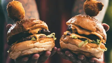 Two cheeseburgers held with fried skewers on top.