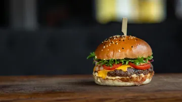 Gourmet burger with cheese and tomato on wooden table.