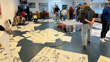 People in art studio with sketches on floor.