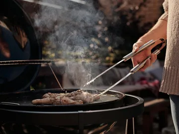 Fleisch wird auf dem Grill zubereitet, umgeben von Dampf.
