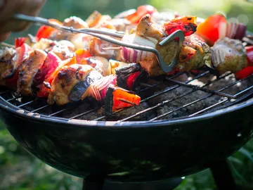 Gegrillte Spieße werden mit einer Zange gewendet, draußen.